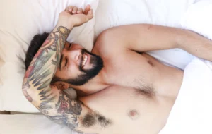 Homem sorridente deitado na cama após desbloquear energia sexual masculina com massagem tântrica, transmitindo bem-estar, prazer e relaxamento.