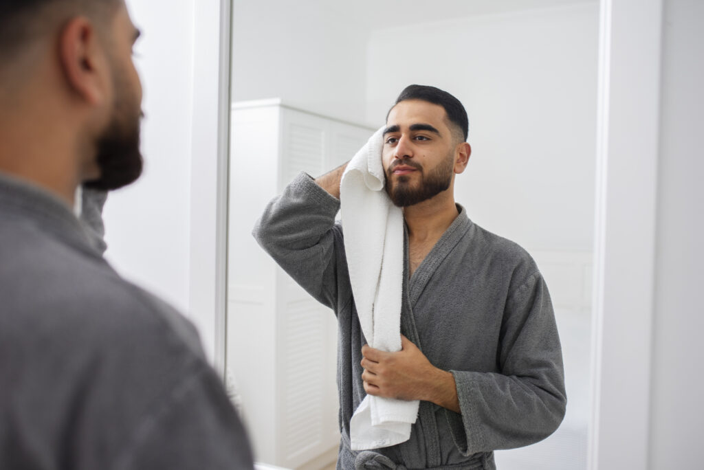 Homem se olhando no espelho após momento de autocuidado, inspirado pelos benefícios da massagem sensual para a autoestima e valorização do corpo.